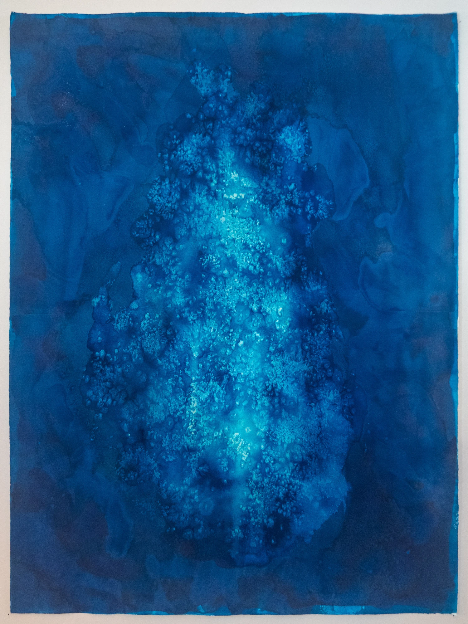 Deep blue field with a single tall luminous granular column running vertically down the center, dissolving into a soft aureole at its edges.
