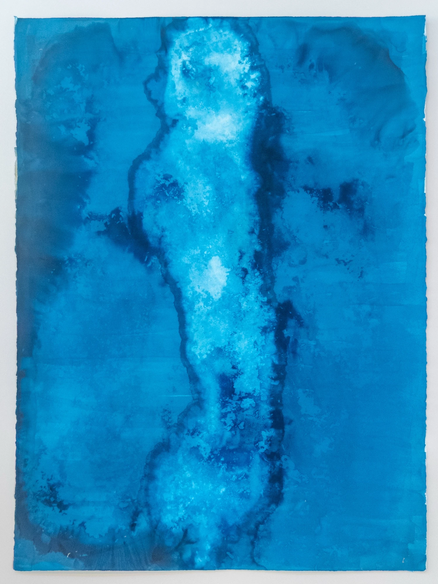 A pale sinuous spine running the full height of the sheet, its edges dissolving into flocculent bloom, held in an even mid-blue field like a breakwater seen from the air through moving water.
