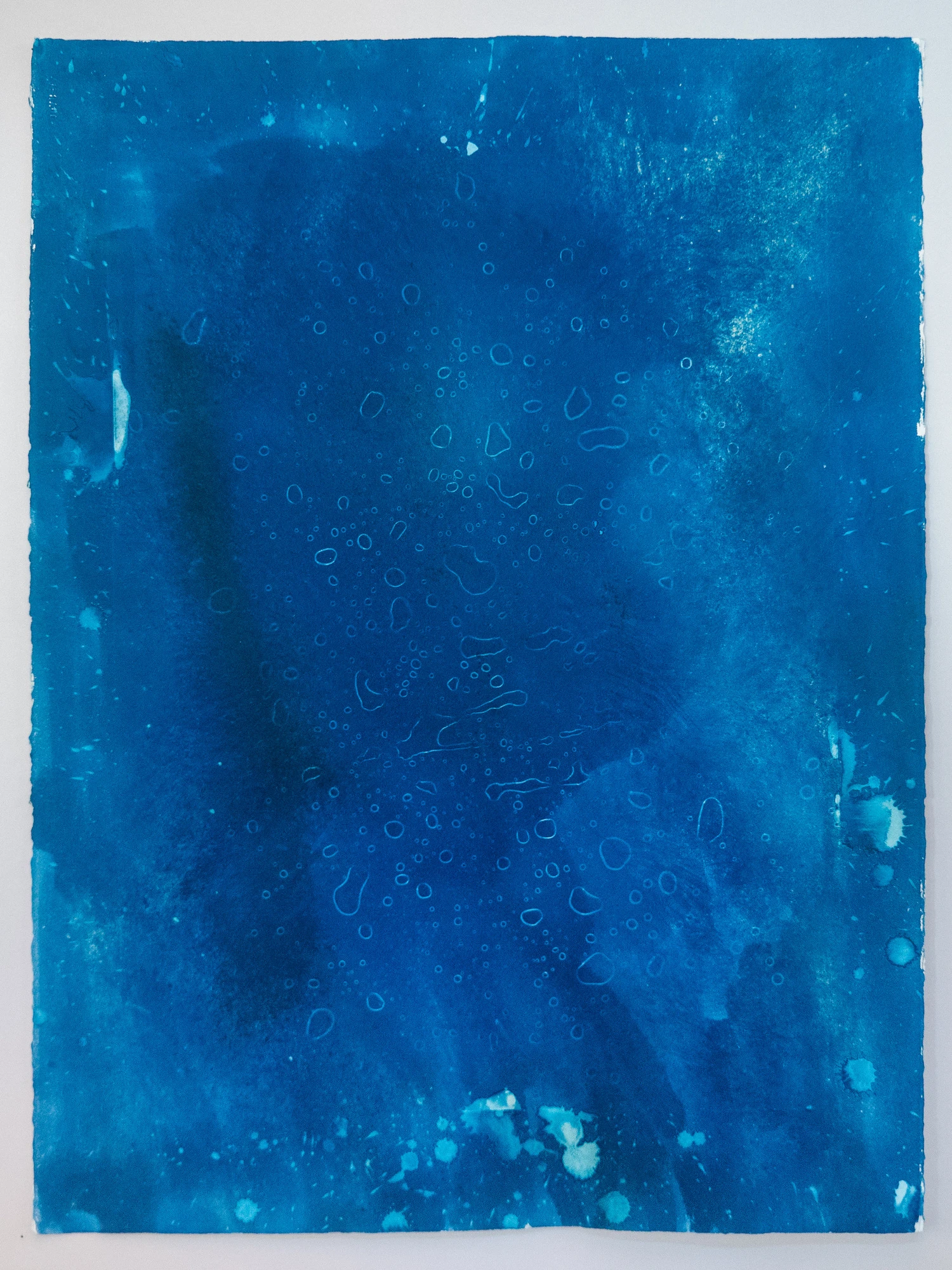 Scattered fine ringed droplets held on an even mid-blue field, rain beaded on a curved surface.
