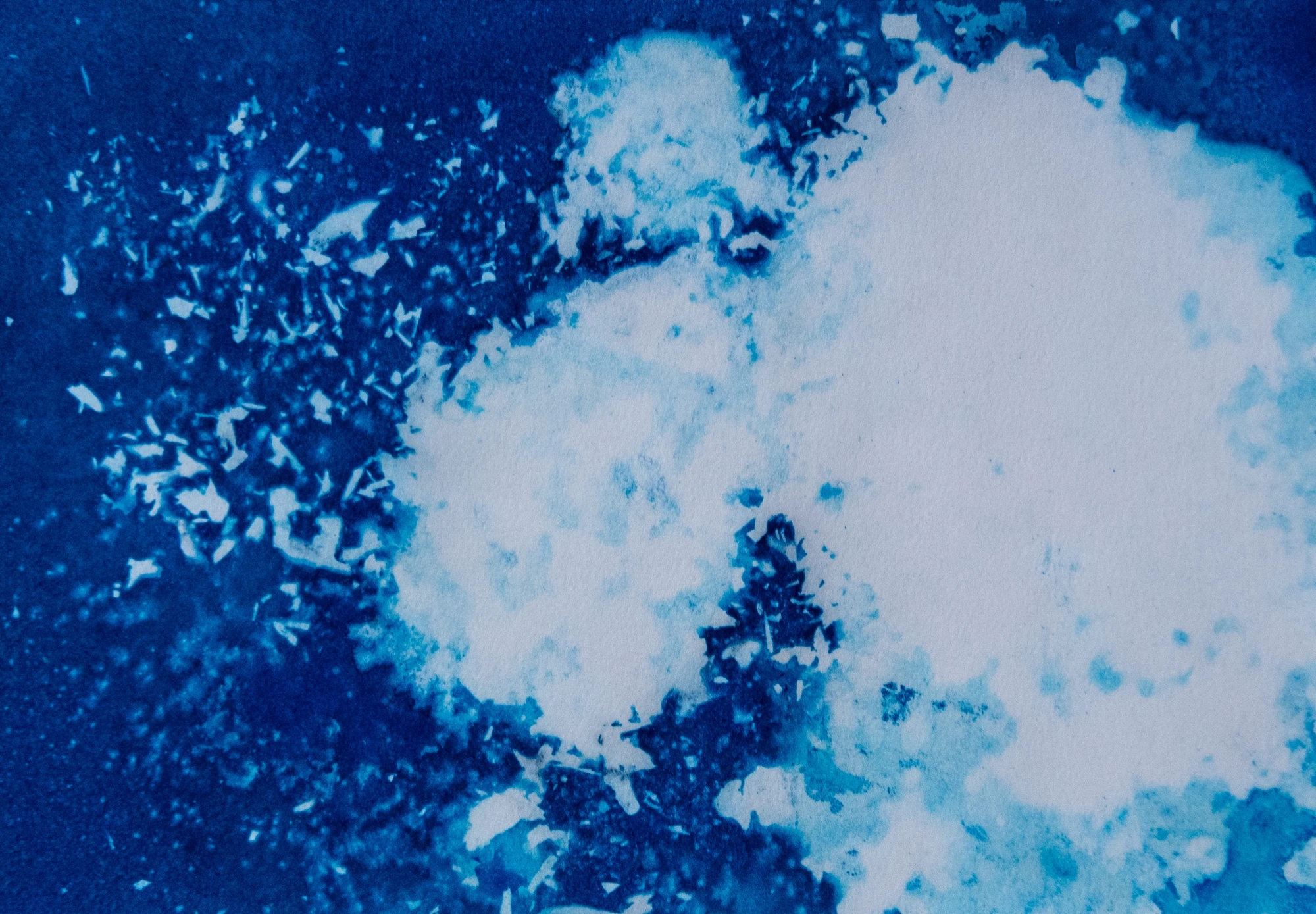 A pale cloud of foam breaking open across deep blue, its left edge scattering into flecks like spray thrown off a curling wave.
