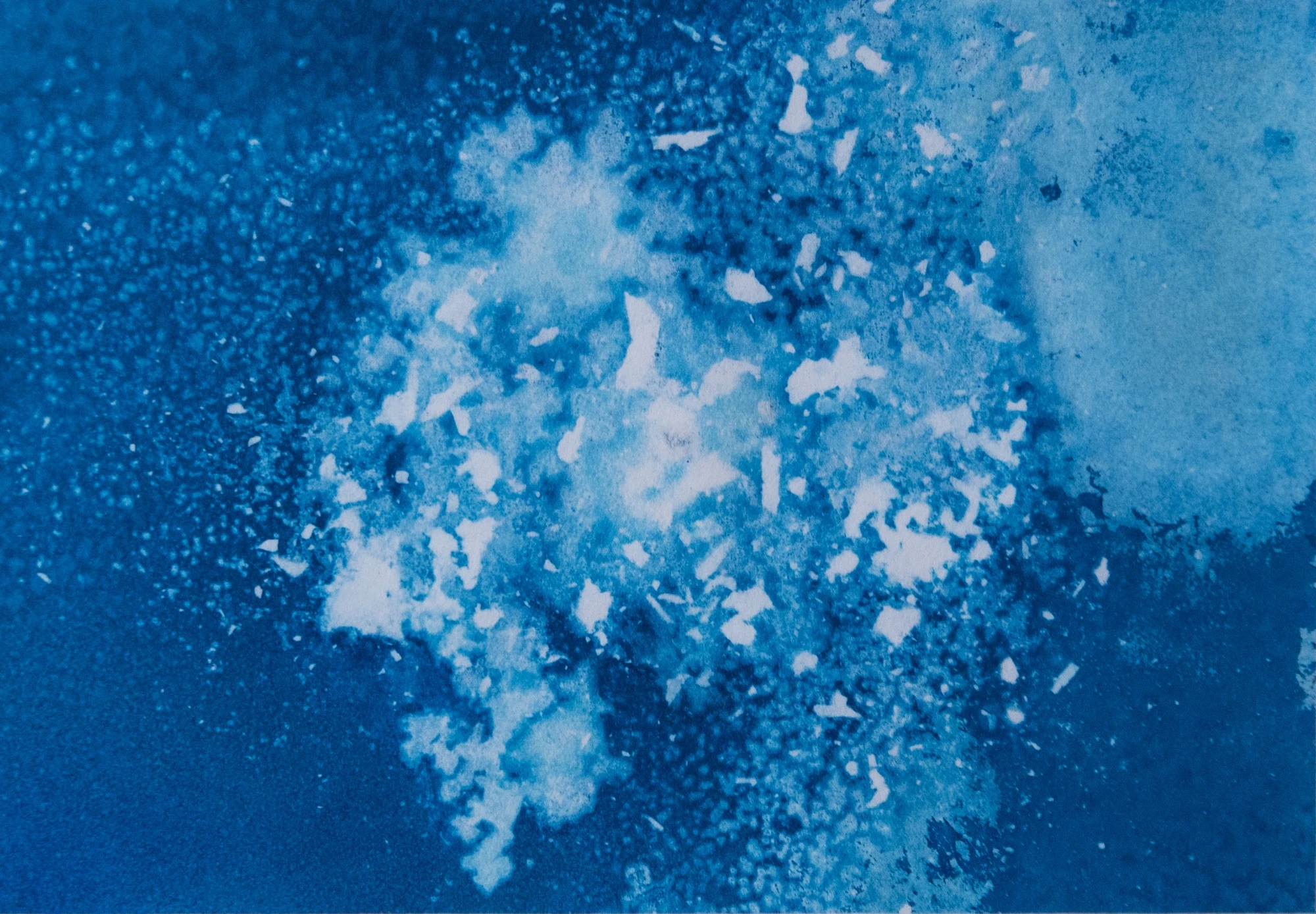 Bright fragments suspended through a grainy blue field, the foam of the first sheet dispersed and sinking rather than breaking.
