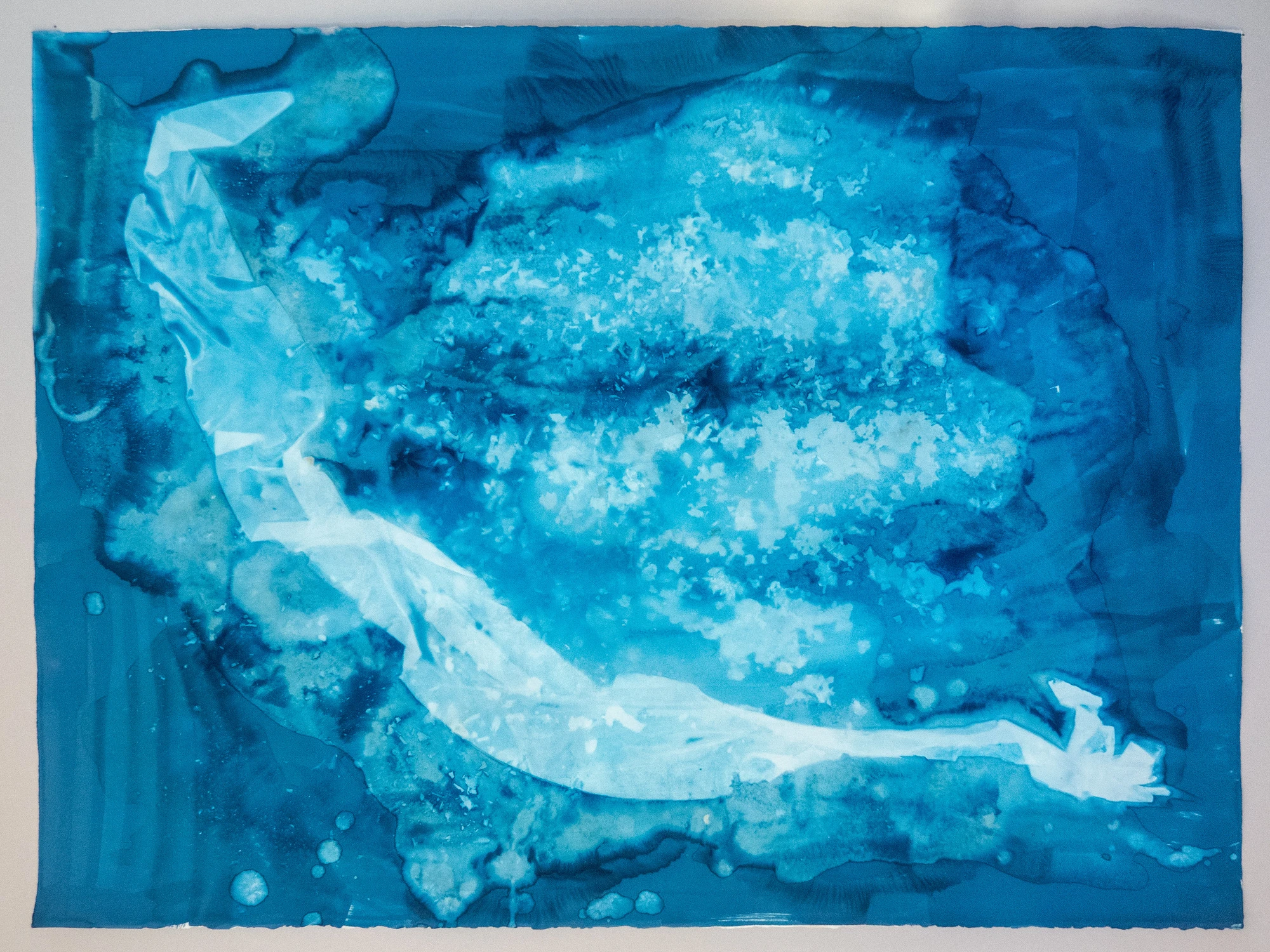 A broad pale flooded basin edged in darker blue, a bright channel sweeping in from the lower right as water arrives across a flat.
