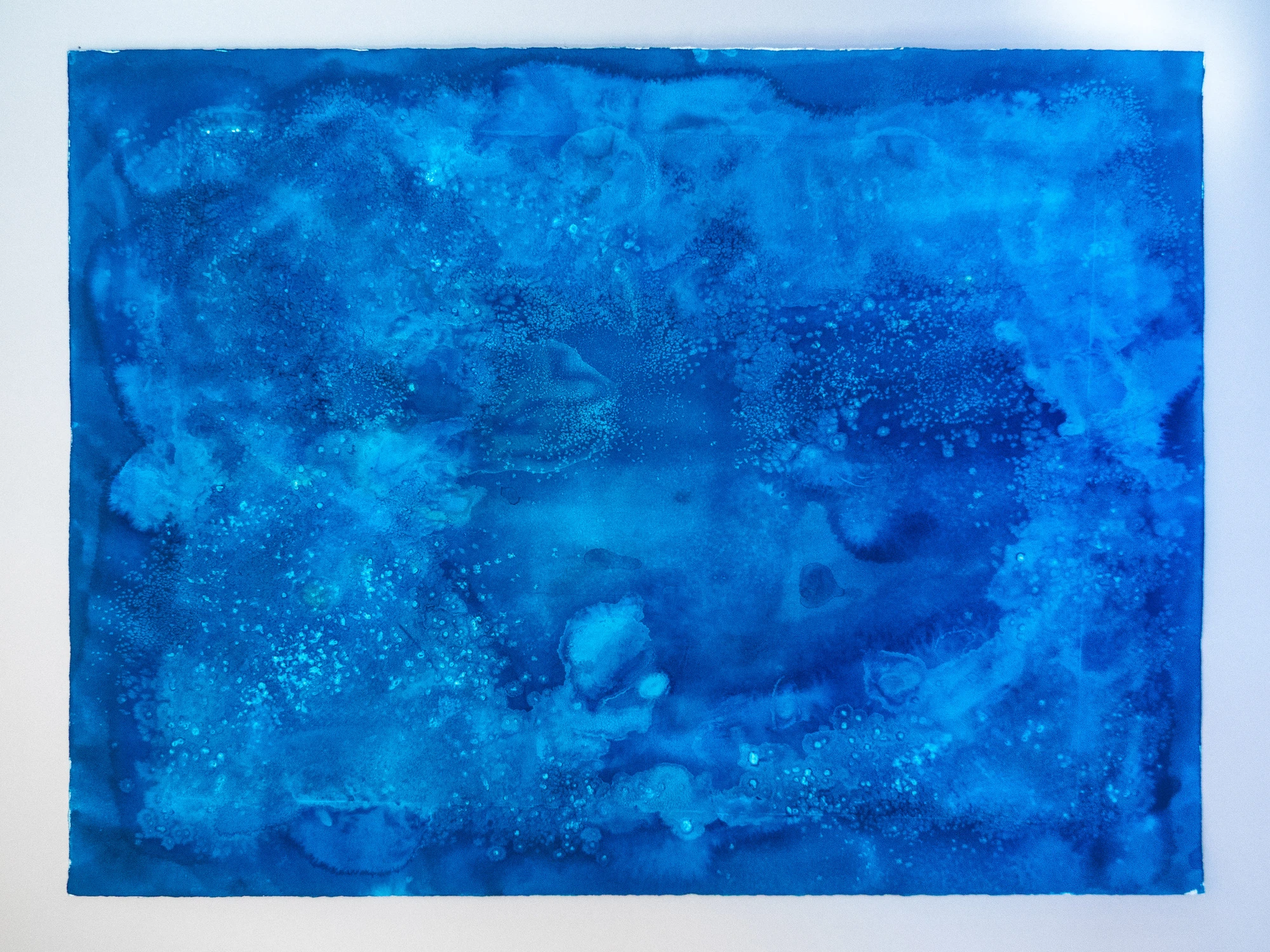 Rounded pale basins pooled against darker blue rock forms, water held in shallow depressions after a tide has dropped.
